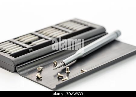 Gray screwdriver and various screws are positioned on a black case with multiple driver bits, all against a white background. The scene is well-lit, d Stock Photo