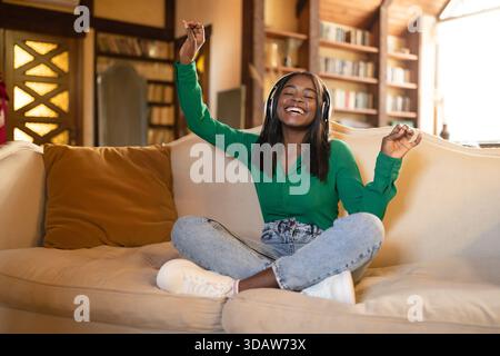 Young Woman Enjoys Music on a Cozy Sofa While Smiling and Dancing in a Bright Living Room Stock Photo