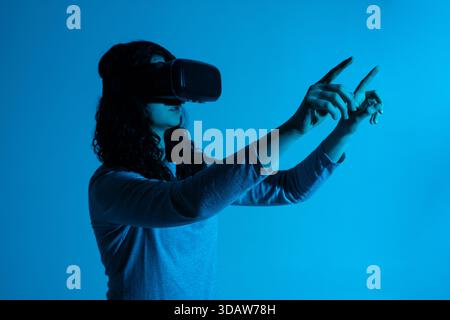 A woman interacts with a virtual interface, reaching outward with both hands while wearing a VR headset Stock Photo