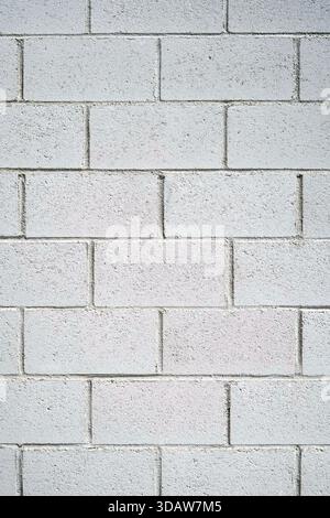 A close-up view of a textured concrete block wall displaying uniform light gray bricks arranged in a neat pattern, providing a minimalist aesthetic su Stock Photo