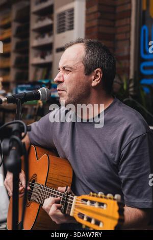 A male musician passionately performs live music at a concert, playing an acoustic guitar and singing into a microphone, creating an engaging musical Stock Photo