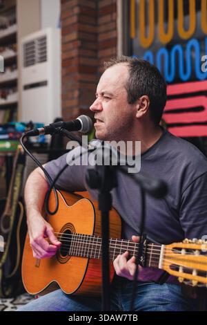 A male guitarist passionately plays an acoustic guitar while singing into a microphone at an intimate indoor live music concert. Vibrant artwork decor Stock Photo