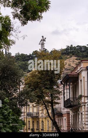 Panoramic view of Tbilisi, Georgia, showing beautiful architectural facades in the foreground and a prominent statue of Mother Georgia on a hill overl Stock Photo
