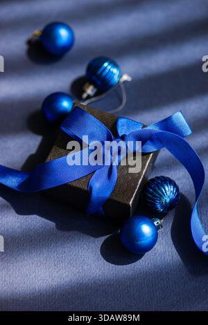 A beautifully wrapped blue Christmas gift box with a matching blue ribbon, surrounded by shiny blue ornaments, creating a festive and elegant holiday Stock Photo