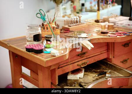 A detailed view of a jewelry workbench filled with tools and materials. The wooden surface is scattered with various crafting supplies, showcasing an Stock Photo
