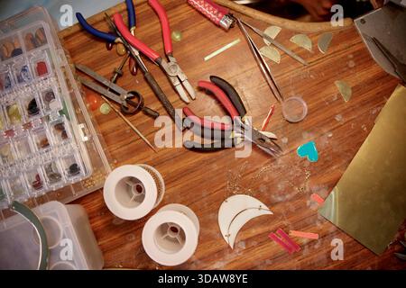 A variety of jewelry crafting tools and materials neatly arranged on a wooden workbench. Includes pliers, wire cutters, beads, and metal shapes, ideal Stock Photo
