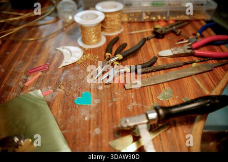 A collection of artisan tools and materials for jewelry making, including pliers, wire, and decorative elements, displayed on a wooden table, showcasi Stock Photo