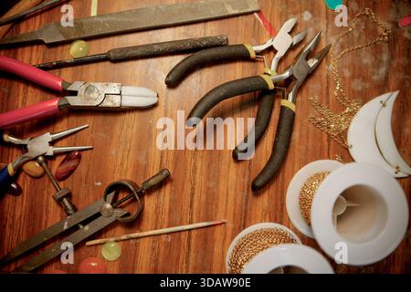 A collection of artisan tools and materials for jewelry making displayed on a wooden surface. Pliers, wires, and decorative elements showcase the craf Stock Photo