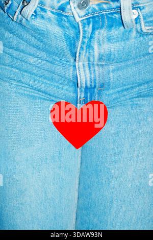 Red heart paper symbol prominently nestled against the blue denim fabric of jeans, representing love and affection with a vibrant contrast that highli Stock Photo