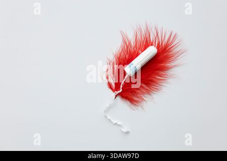 A close-up view of a white tampon resting on a vibrant red feather, symbolizing menstruation, periods, and feminine hygiene products in a conceptual d Stock Photo
