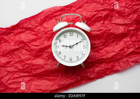 A white alarm clock set against a red textured background represents the concept of time and menstruation cycles, highlighting the natural rhythm and Stock Photo