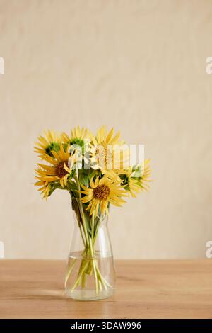 A vibrant bouquet of sunflowers elegantly arranged in a clear vase, set on a wooden table within a warm and cozy home environment. Perfect still life Stock Photo