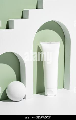 A sleek white cosmetic tube is elegantly positioned on a minimalist geometric podium. The soft green and white background enhances the sophisticated a Stock Photo