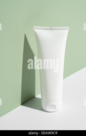 A sleek, white cosmetic tube stands vertically on a white surface against a soft green background. The composition highlights simplicity and elegance, Stock Photo