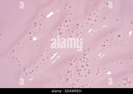 A smooth layer of pink cosmetic cream texture with delicate bubbles spreads across a soft pink background. The glossy surface reflects light, creating Stock Photo