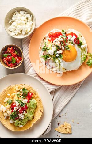 Top view of two plates with Rancheros eggs. One features a sunny-side-up egg on tortilla with fresh veggies, served on orange ceramic. The other has s Stock Photo
