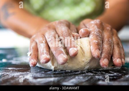 Cropped unrecognizable hands kneading dough on a flour-dusted surface, preparing bread for baking, highlighting the process of making homemade bread. Stock Photo