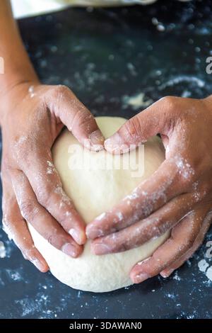 Cropped unrecognizable woman skillfully shaping bread dough with flour-dusted hands, preparing it for a delicious baking session in the kitchen. Stock Photo