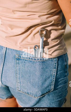 A woman stands on the roadside in Australia with a broken down car, holding some wrenches. The sunlight highlights the rural landscape background. Stock Photo