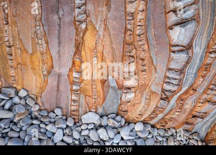 A stunning view of layered rock textures meeting smooth pebbles. The contrast between the rigid rock formations and the round stones creates a captiva Stock Photo