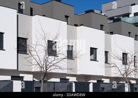 A modern townhouse exterior featuring a minimalist design with sleek white walls and contrasting dark window frames. The architectural style is contem Stock Photo