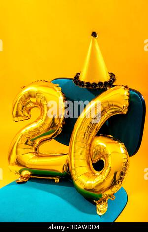Golden foil number balloons form 26 with a festive party hat on a vibrant background. Perfect for celebrating events like birthdays, New Year, or anni Stock Photo