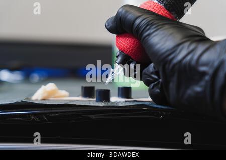 Female tattoo artist working diligently during a session, wearing black gloves while holding a tattoo machine. Various tools are neatly arranged, show Stock Photo