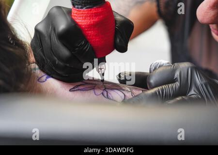 A skilled female tattoo artist focuses intently as she creates intricate designs on a client's skin, using precision tools in a professional studio se Stock Photo