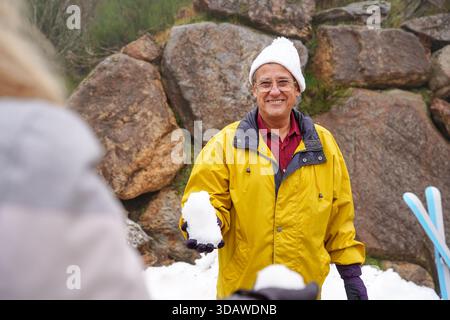 An older couple joyfully engaging in winter activities, surrounded by snow and rocks. The man playfully holds a snowball, capturing the essence of fun Stock Photo