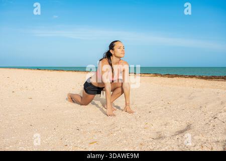 A serene scene of a young woman practicing yoga by the shoreline in Colombia. The peaceful beach setting enhances the sense of tranquility and focus d Stock Photo