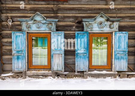 View of intricate blue window frames against the rustic, weathered log cabin, peeking through the glass in Irkutsk, Irkutsk Oblast, Russia. Stock Photo