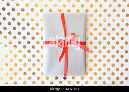 Minimalistic gift box with red ribbon on white and gold polka dot background. Festive, bright and modern composition. Perfect for holidays or celebrat Stock Photo