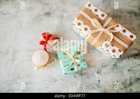 Christmas gift wrapping flat lay with elegant presents, rustic ribbon, candles, and polka dot paper on concrete background. Cozy, festive atmosphere w Stock Photo