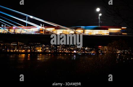 View of the train streaks across the bridge at night, lights blurring into streaks of white and blue, reflecting off the dark water below, tilikum bri Stock Photo