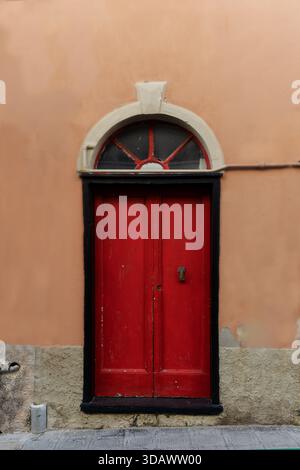 Red wooden door set in an old plastered wall, Italy Stock Photo