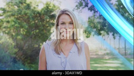 Standing woman in sleeveless striped blouse smiling at camera in garden with lawn, blue streak Stock Photo