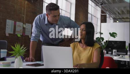 Working woman in mustard top and blue shirt man reviewing laptop at loft office, with succulent Stock Photo