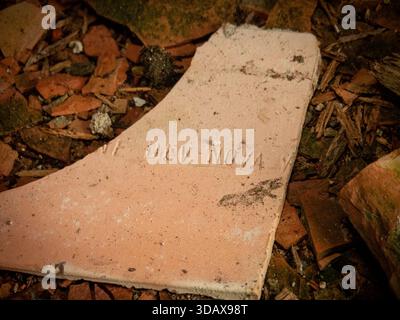 Broken ceramic tile fragment with faint lettering among rubble inside an abandoned building Stock Photo