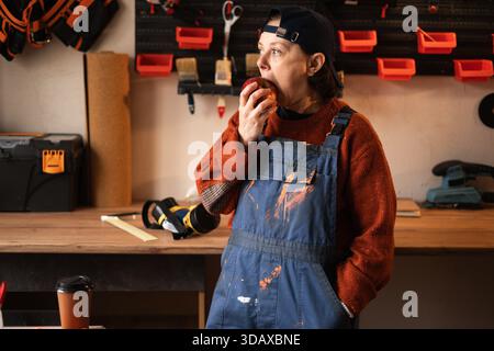 repairwoman or female mechanic eating food in her repair shop or garage Stock Photo
