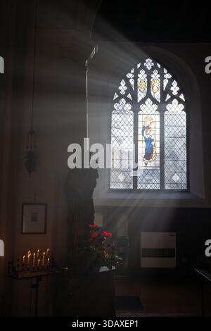 Norwich, Norfolk, UK: Church interior with a statue of Mary and Jesus. Sunlight streams through the window. Candles and flowers complete the scene. Stock Photo