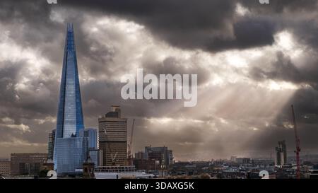 The Shard skyscraper stands tall against a dramatic, cloudy sky with sunbeams breaking through, symbolizing London's modern architecture amidst changi Stock Photo