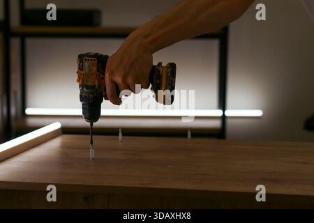 Focused shot on hand gripping drill to fasten screw in wood, several nails waiting on surface Stock Photo