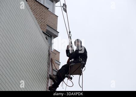 A worker in a harness performs maintenance on a high-rise building, suspended mid-air. Kyiv, Ukraine. December 12, 2025. Stock Photo
