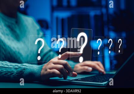Concept of online question and answer, problem-solving, and digital communication. Person using laptop touching question mark icons symbolizing curios Stock Photo