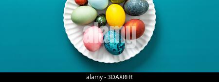 Festive, colorful eggs in various shades are neatly arranged on a decorative plate, symbolizing Easter traditions and spring celebrations with vibrant designs, banner Stock Photo