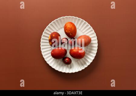 Vibrant Easter eggs in various shades of red and orange are beautifully arranged on a white plate, adding charm to the festive atmosphere of the season Stock Photo