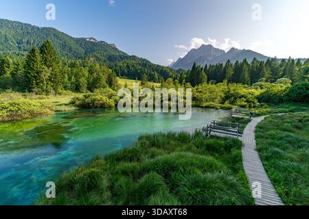 Serene walk along a wooden path beside the tranquil waters of Slovenias Zelenci Nature Reserve, surrounded by lush greenery and towering mountains nea Stock Photo