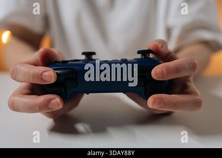 Close-up cropped shot of unrecognizable female gamer holding blue wireless video game controller, representing concepts of entertainment, leisure Stock Photo