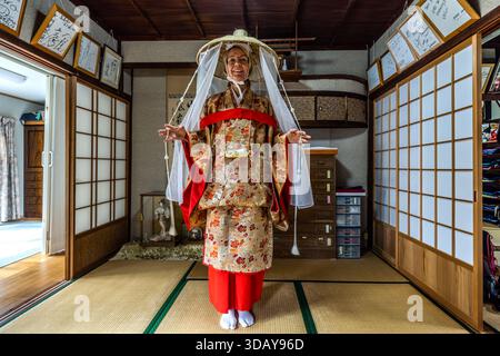 A tourist stands ready in a rented Heian-style kimono with a wide straw hat and veil in Nachikatsuura, Wakayama Prefecture, Japan. She plans to walk part of the Kumano Kodo pilgrimage route dressed this way. Stock Photo