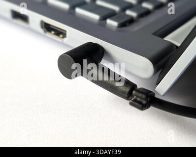 close up of hand plugging round charging cable into laptop power port Stock Photo